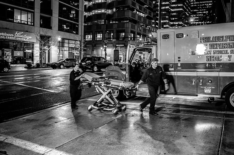 A pair of medics walking with a stretcher near their ambulance.