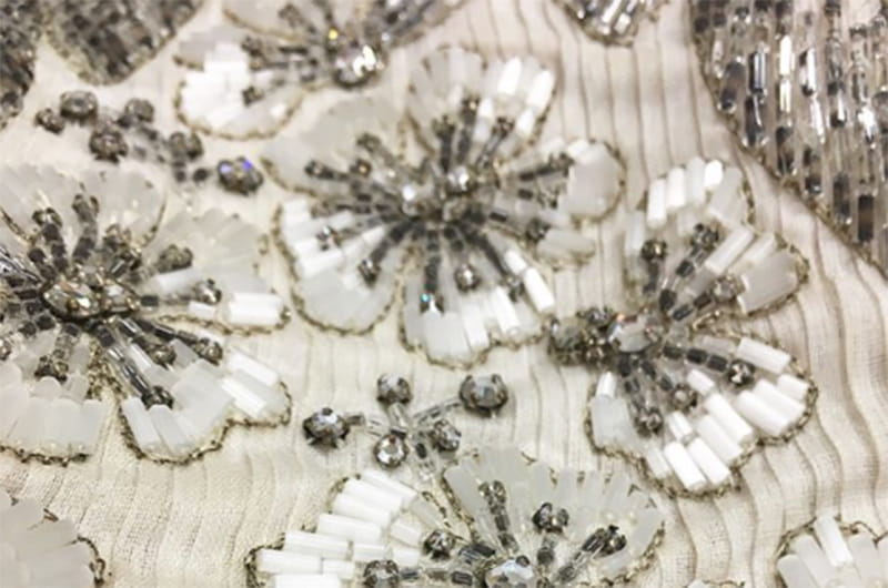 A close-up of an Instagram post that the Fox Historic Costume Collection shared in November of a James Galanos full-length sheath dress from 1955 made with silk satin straps and finely pleated silk organza with white and silver beading.