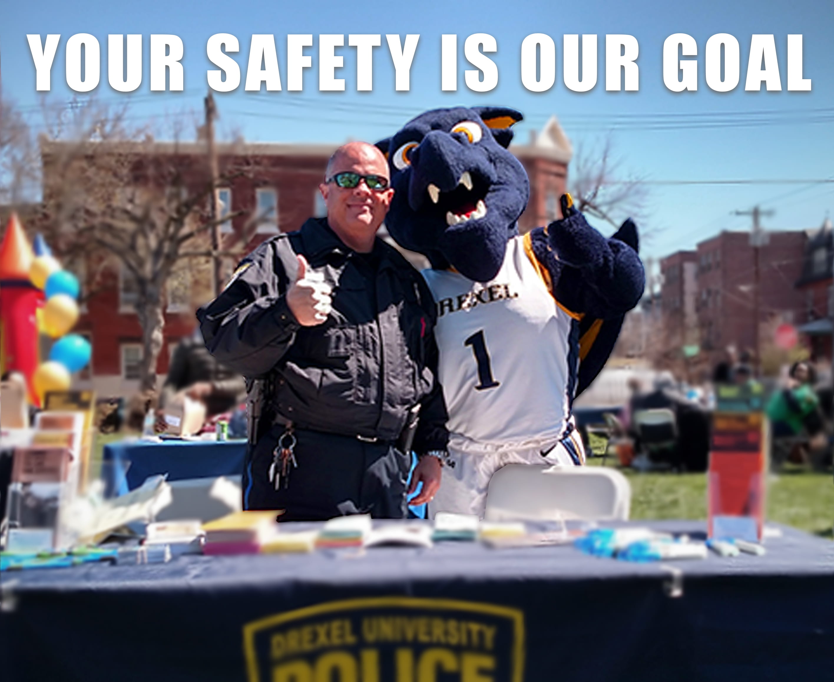 Image of an officer and Mario the Magnificent dragon posing at a table outside with the text "Your Safety is Our Goal."