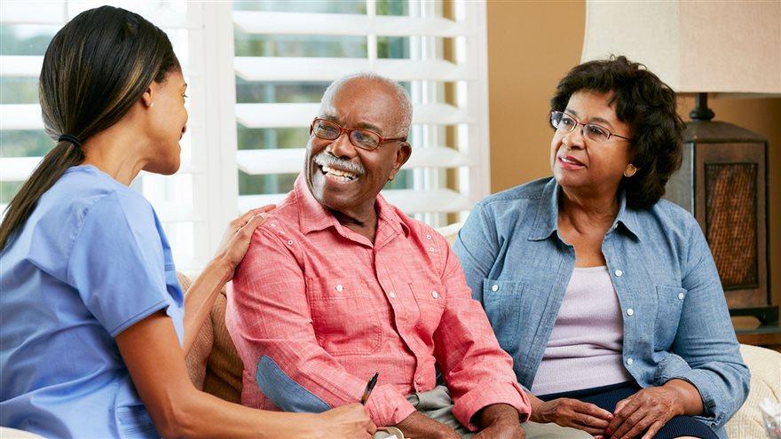 Older man and woman sitting with nurse in home environment