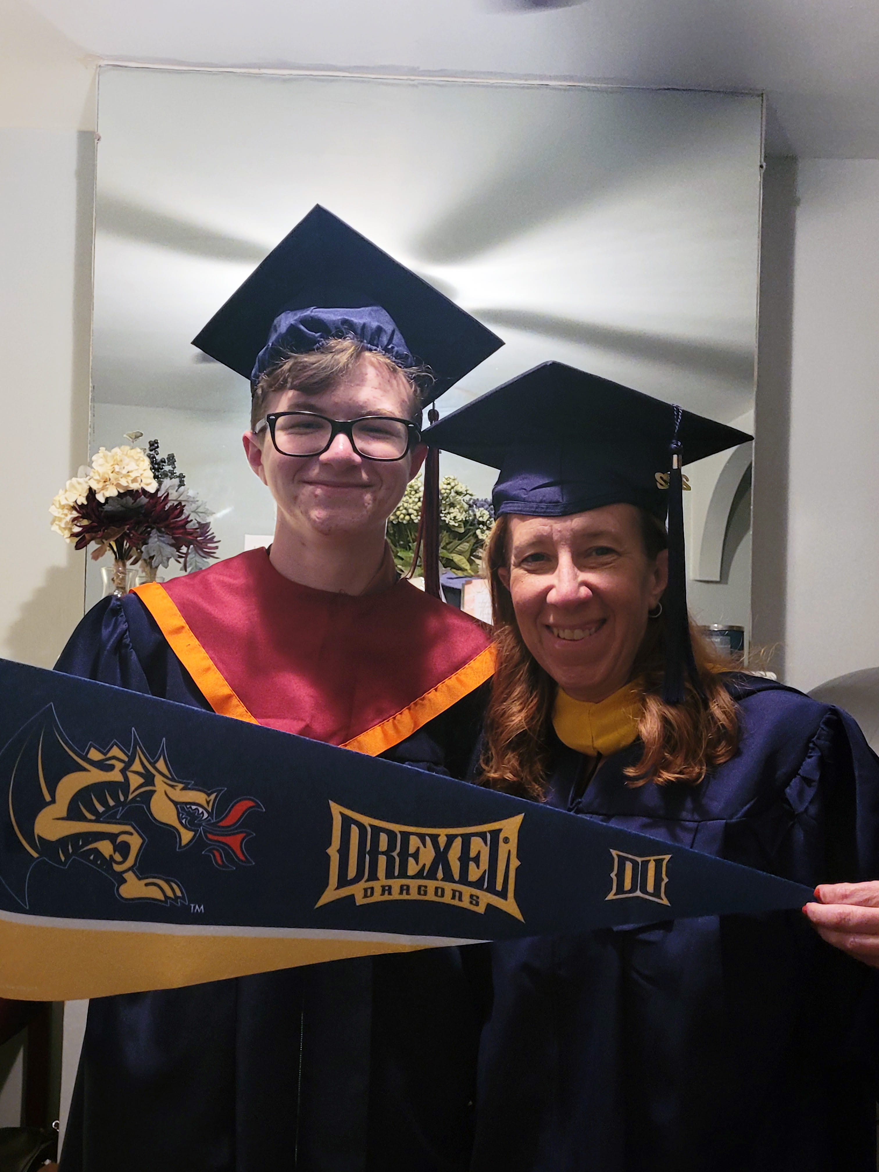 A mother and son in Drexel commencement regalia holding a Drexel pennant.