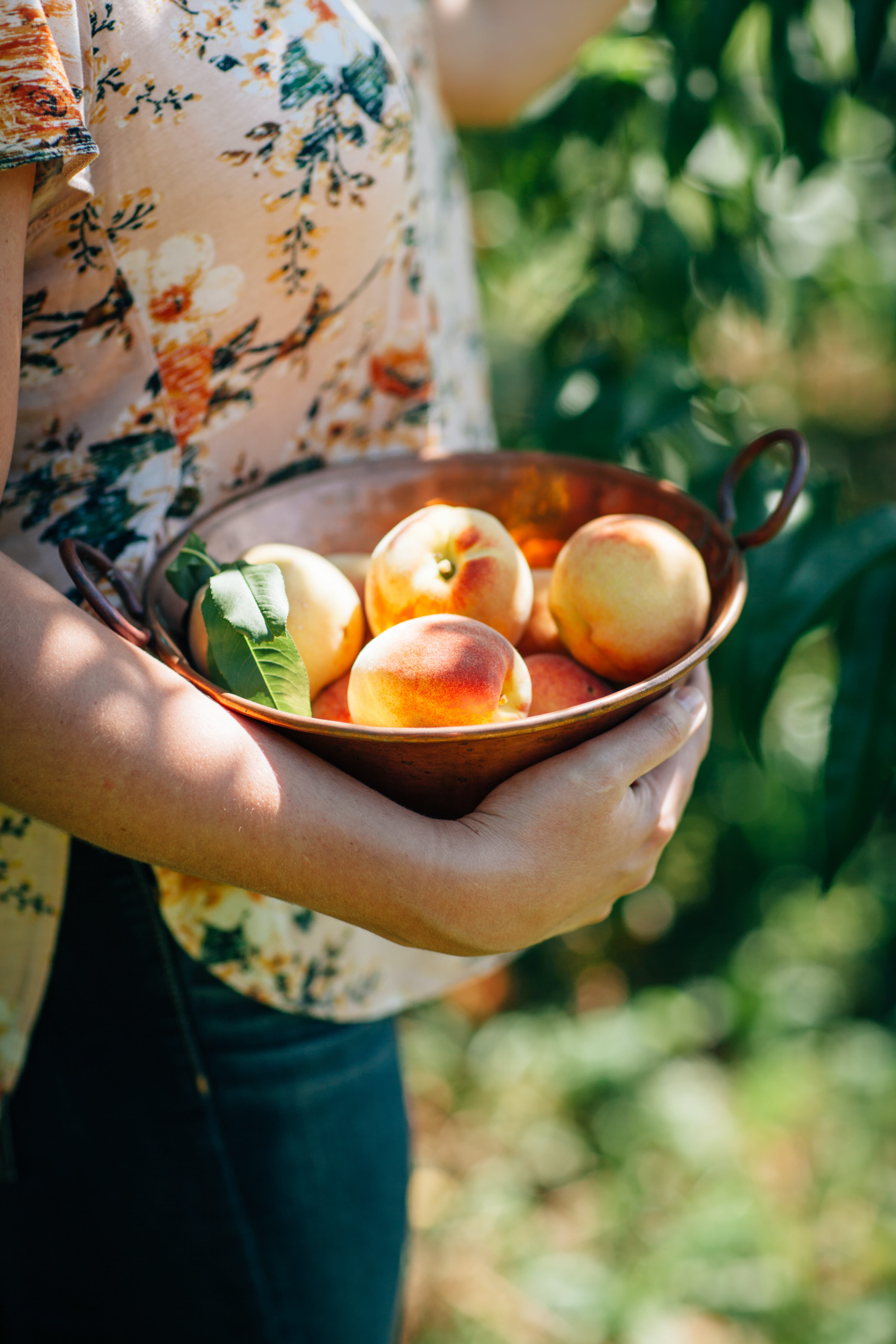 A person holding a bowl of peaches outside.