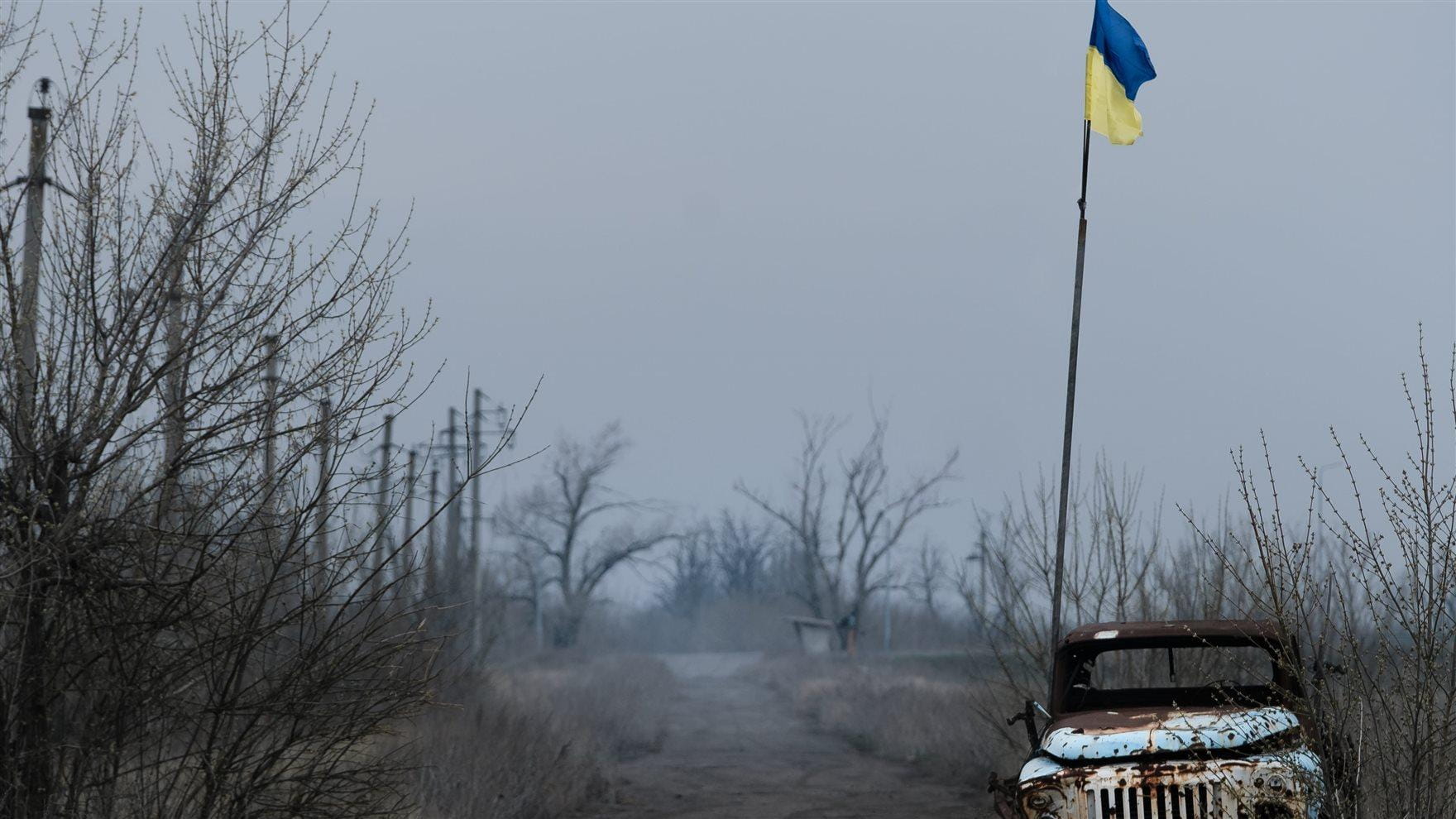 Image of a destroyed Russian vehicle under the Ukrainian flag outside. 