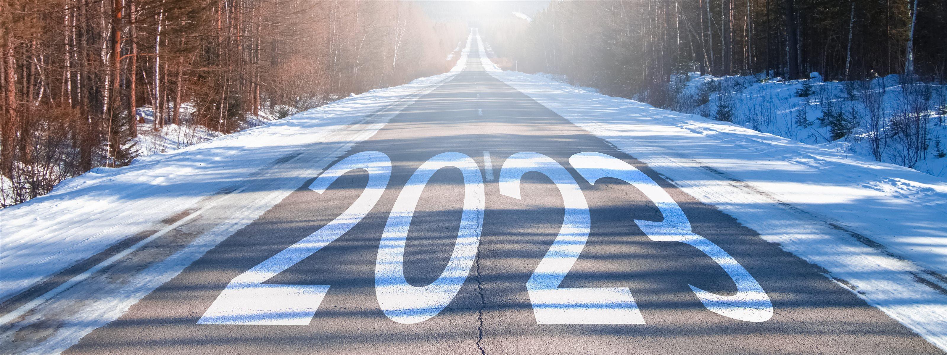 The word 2023 is written on a highway in the middle of an empty asphalt road at dawn and a beautiful blue sky. New year 2023 concept.