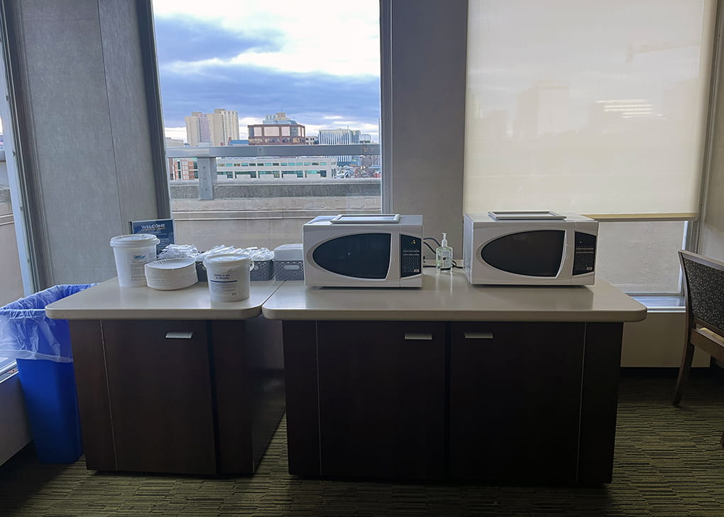 Two microwaves on a table in front of a window.
