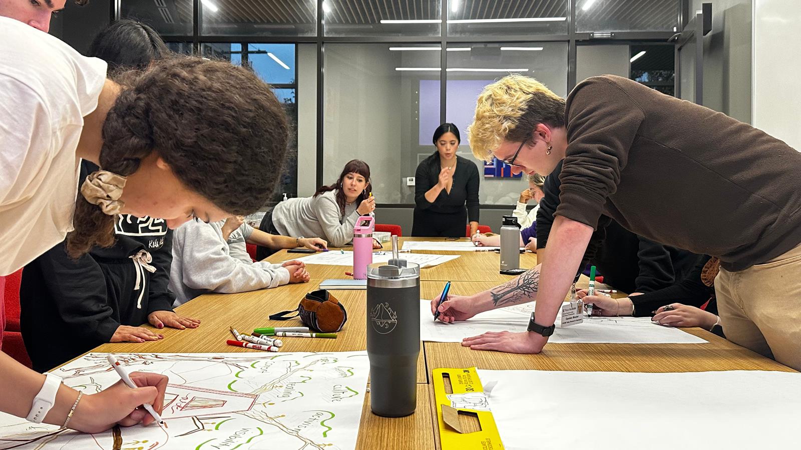 A group of Honors students leaning over a table drawing murals on large pads of paper.