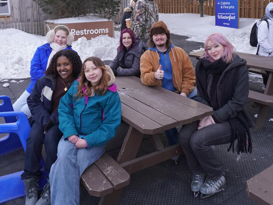 A group of students in winter coats and ice skates sit around a picnic table.
