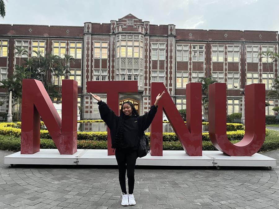 A student standing in front of a university sign