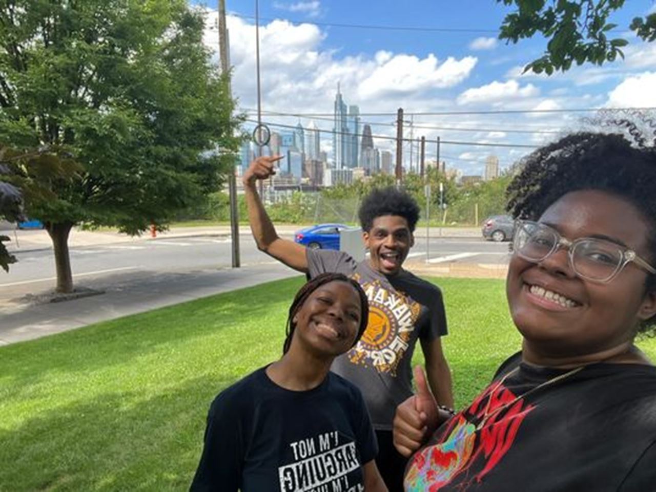 Three STAR Scholars taking a selfie in a park, one of them points at the Philly skyline