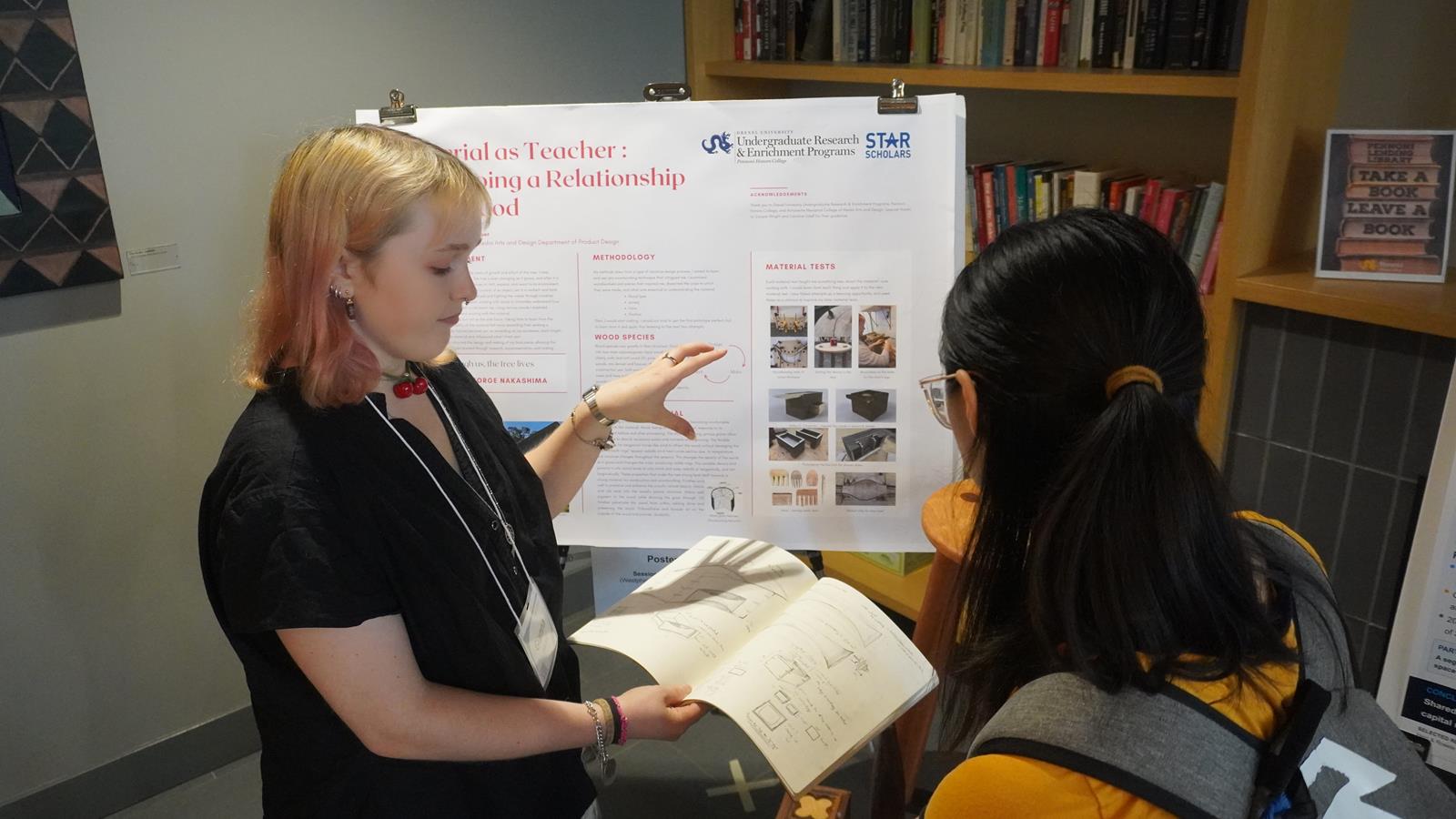 A STAR Scholar shows her research poster and notebook to a student.