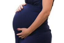 A pregnant woman in a blue dress holding her stomach.