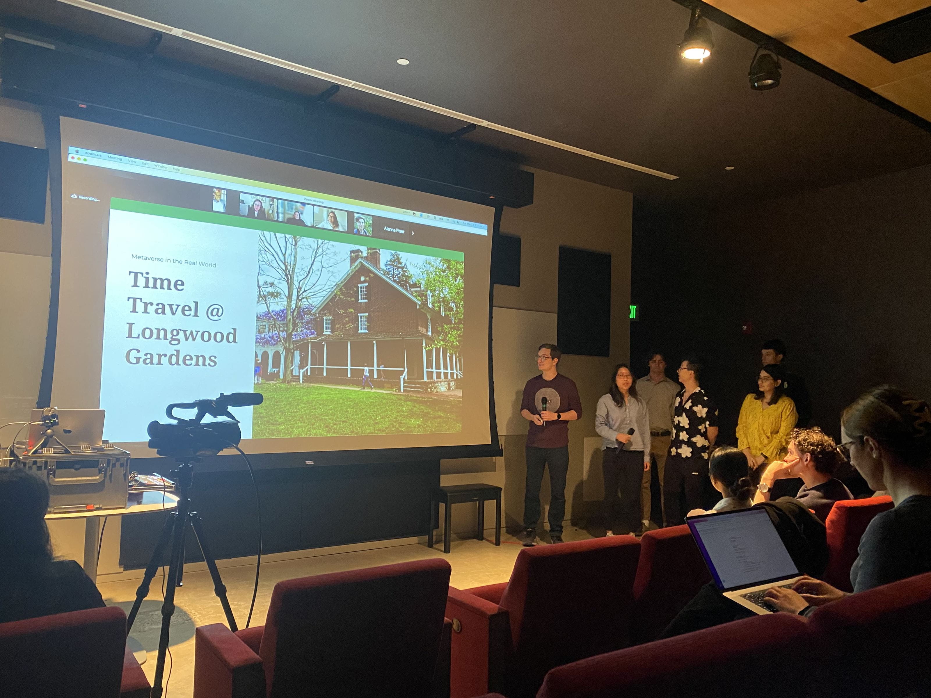 A group of students presenting in front of a projection screen that reads "Time Travel @ Longwood Gardens"