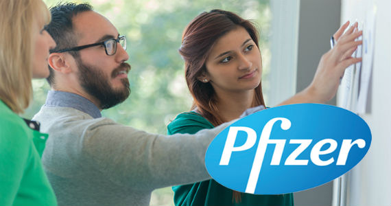 Group of Professionals standing and viewing papers on a wall, Pfizer logo in lower right corner