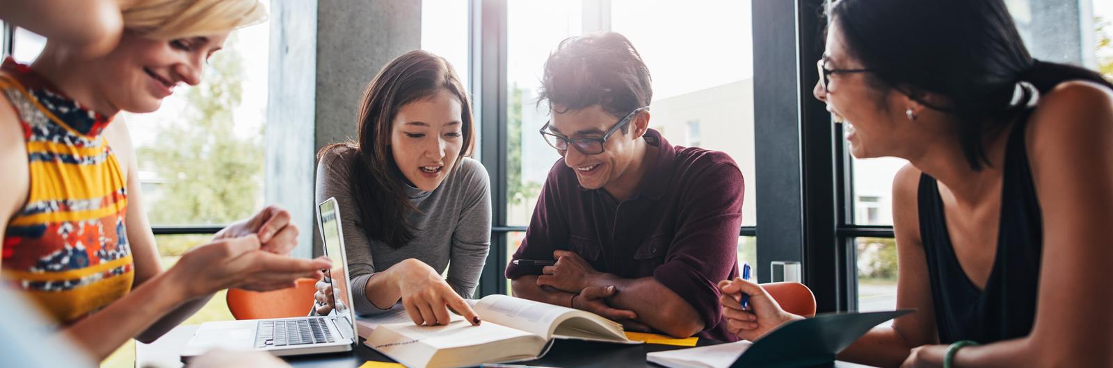 Young students sitting at a table in a library and reading books for their class assignment.
