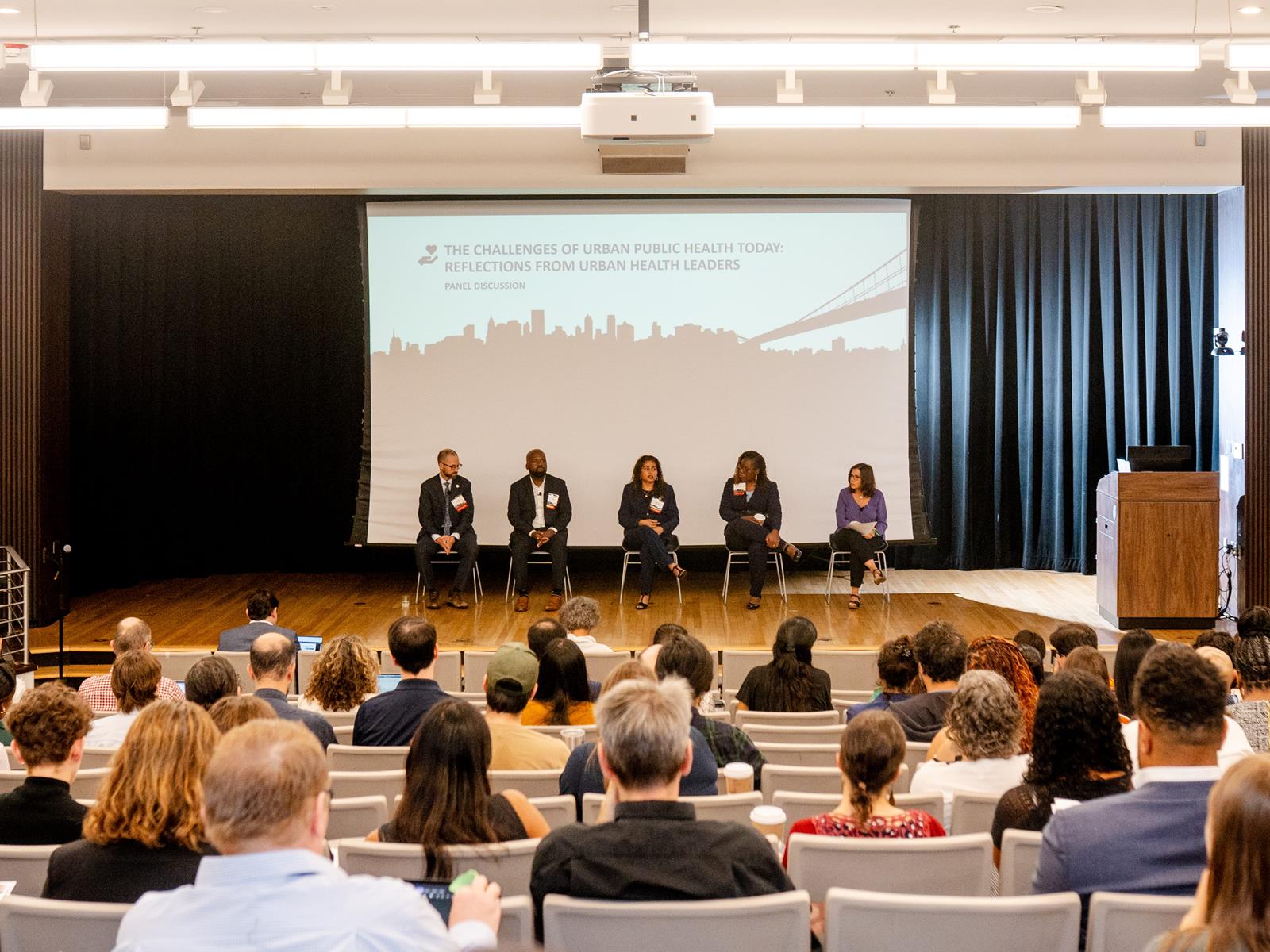 Crowd of attendees in an auditorium listen to panel discussion on stage