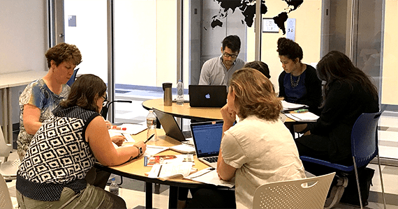 6 people working together around a desk 