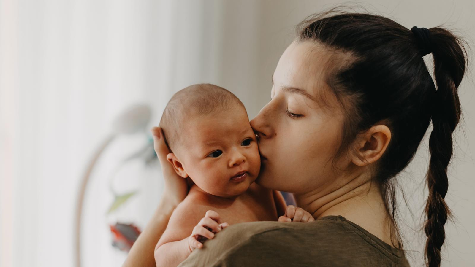 young mother kisses new baby in a nursery