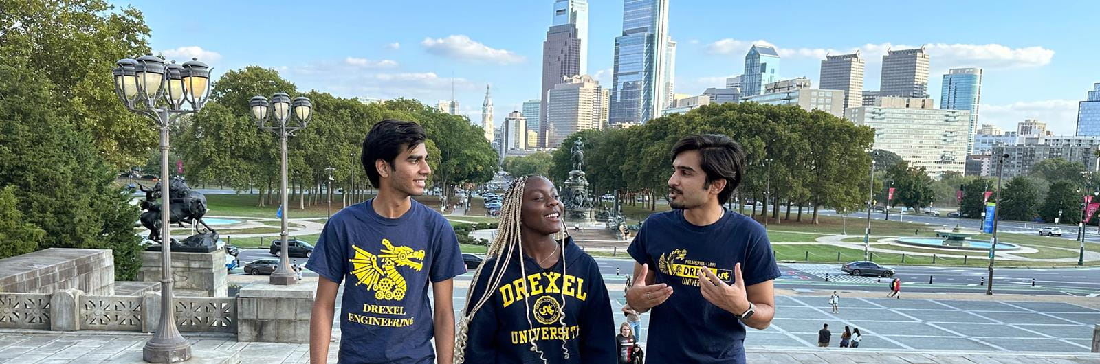 three Drexel students walking up Art Museum steps with Philadelphia skyline in background