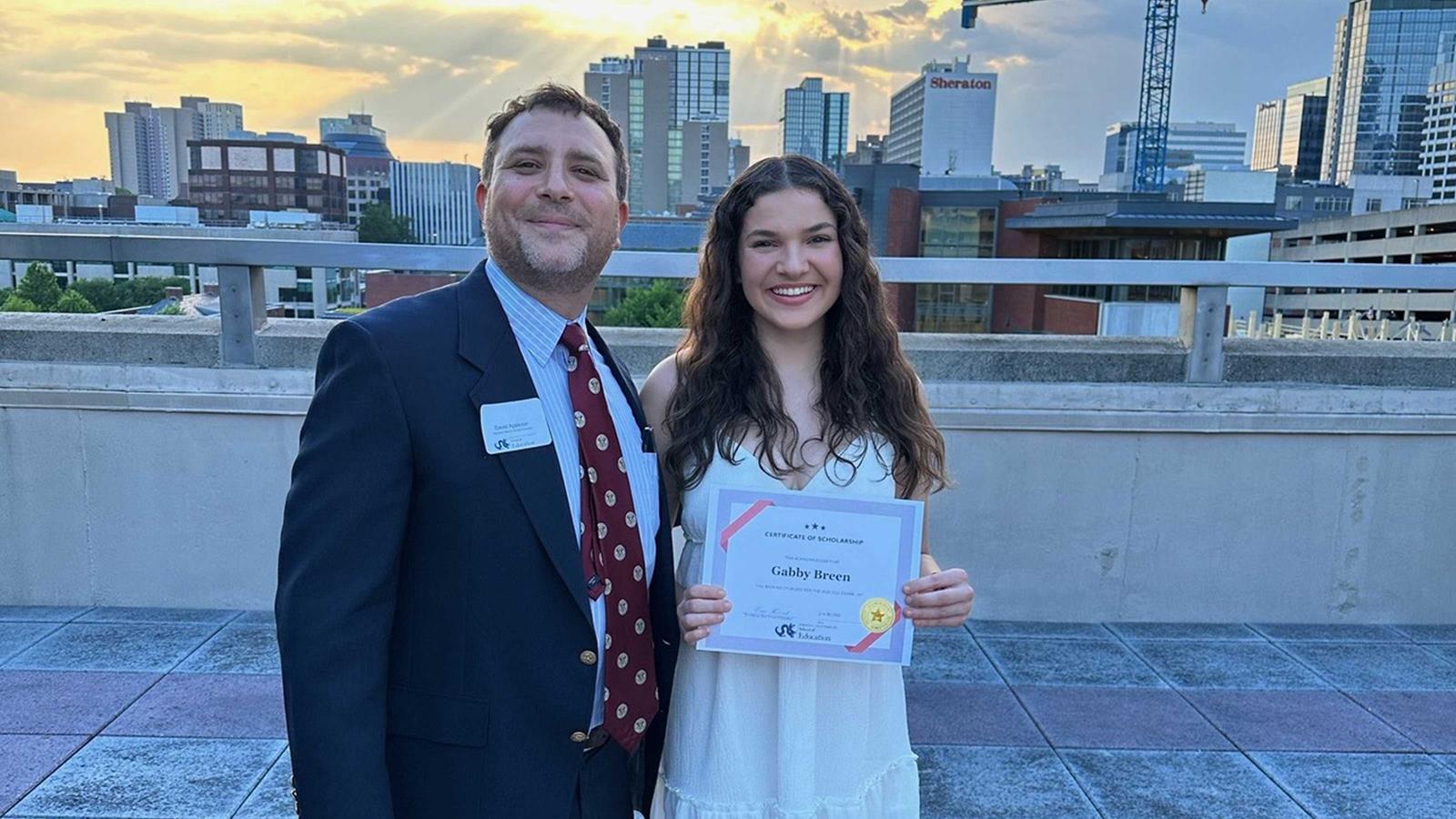 Two people celebrating a certificate of scholarship with the Philadelphia skyline