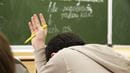 Young boy with his head down raises his hand with a pen.