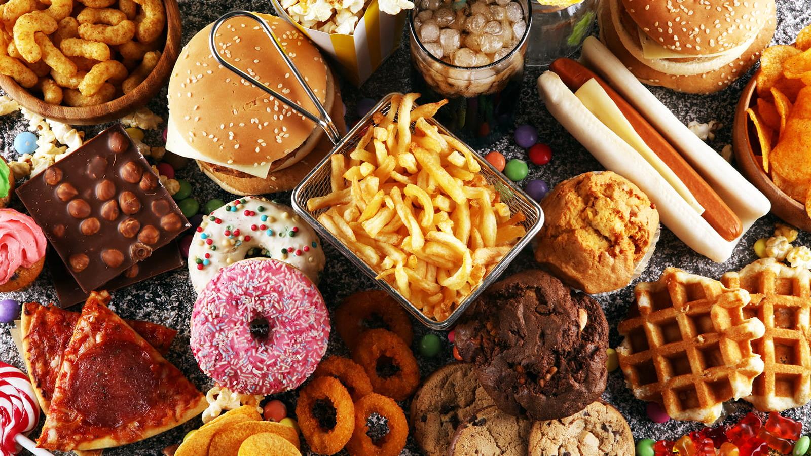 A pile of french fries, burgers, donuts, cookies, chips and other high sugar and high fat foods. 