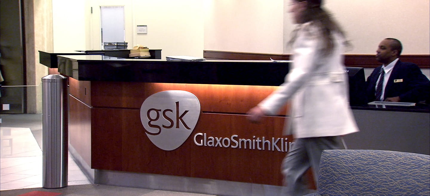 A woman walks past an office's front desk bearing the Glaxo Smith Kline logo.