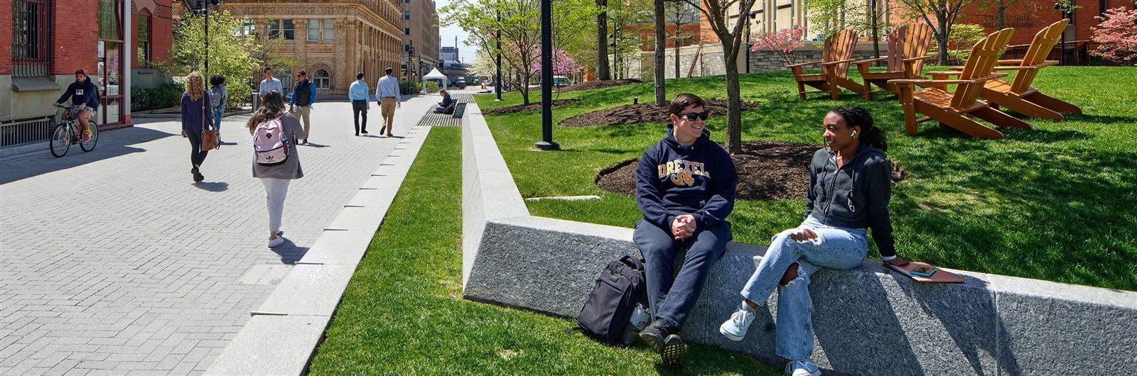 Two students sit chatting outside the Drexel Main Building on Perelman Plaza.