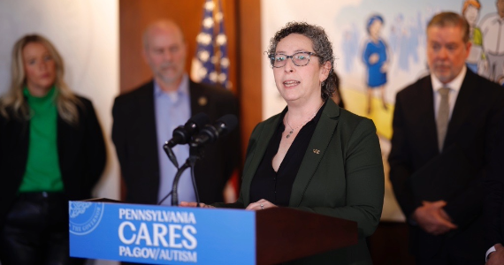 Photograph of Dr. Diana Robins in front of a podium that reads Pennsylvania Cares pa.gov/autism