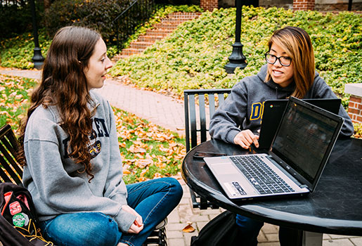 Two students sitting at an outdoor table, working on their laptops 