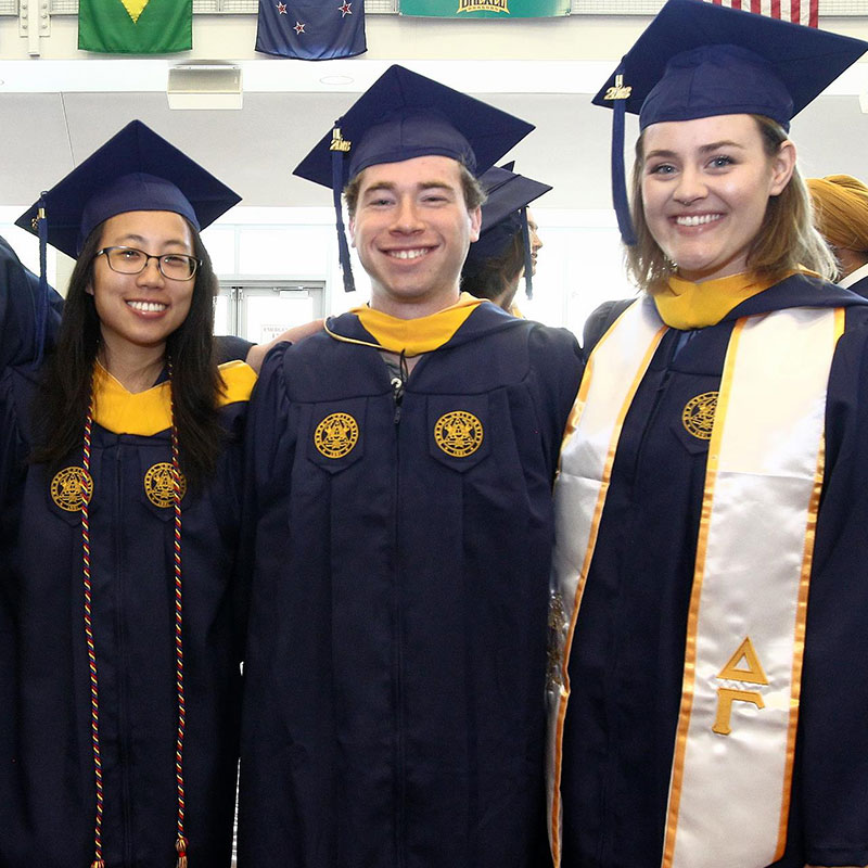 Photo of three students wearing a cap and gown at Drexel's Commencement Ceremony