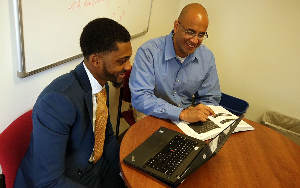 A Drexel student sits at a table with Professor Thomas Heverin, both are looking at a laptop screen