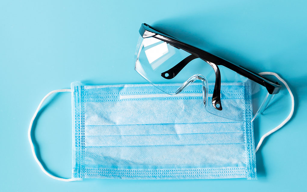 Photo of protective glasses and face mask on light blue background