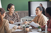 Photo of four women sitting around conference table and talking