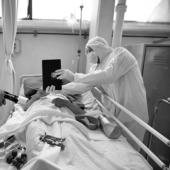 Photo of doctors utilizing artificial intelligence with a patient in a hospital bed using a tablet. 