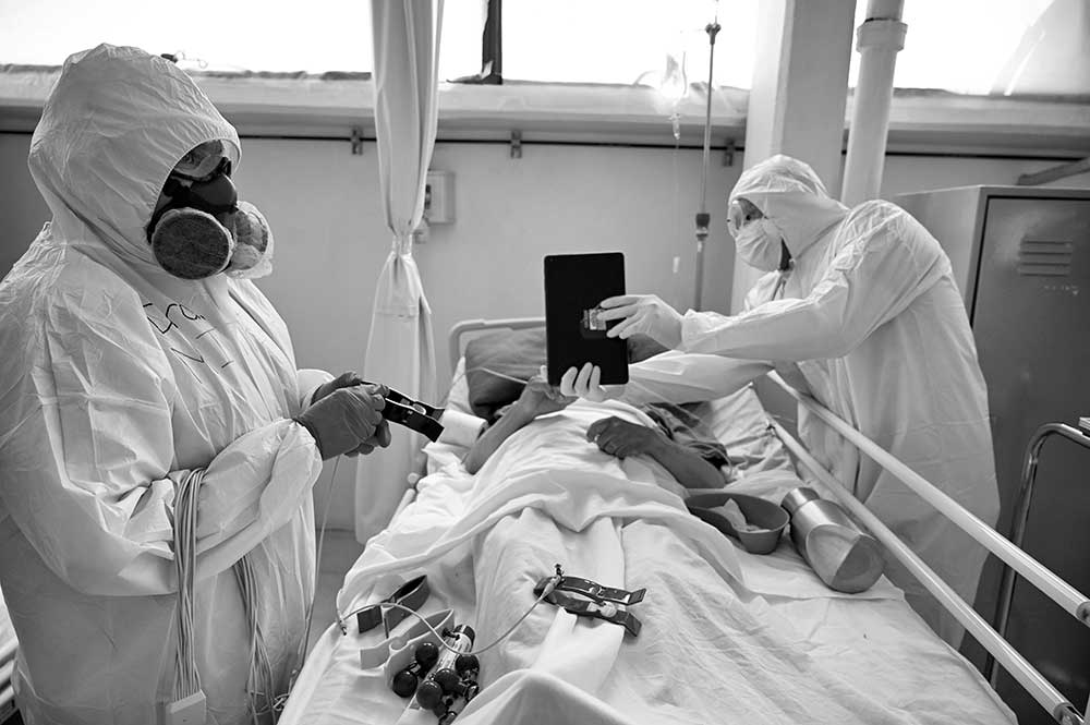 Photo of doctors utilizing artificial intelligence with a patient in a hospital bed using a tablet. 