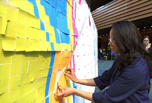 Dalila Wilson-­‐Scott, Senior Vice President for Community Impact at Comcast and President of the Comcast NBCUniversal Foundation adds a Post-­‐it pattern, representing a pixel, to the template that would eventually form a supersized GIF image of the Liberty Bell and Philadelphia Eagles logo by the end of the activity.