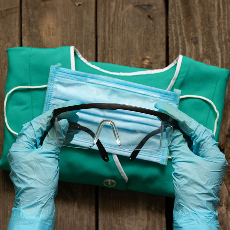 Photo of hands wearing blue latex gloves holding protective glasses over scrubs