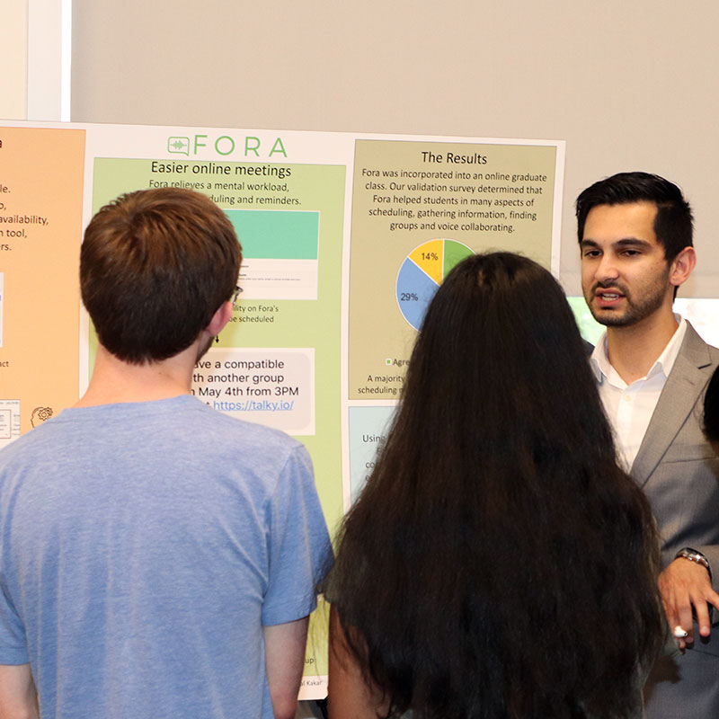 Photo of student presenting Senior Project poster to two people