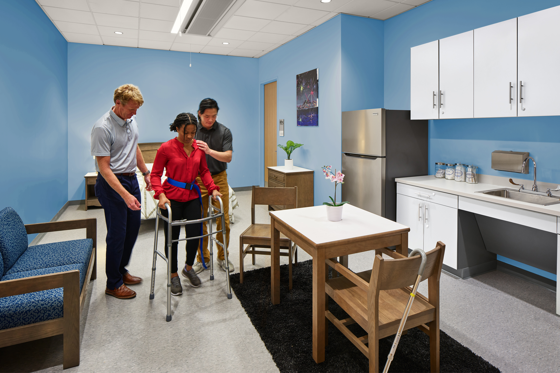 two health care professionals assist a patient using a walker to navigate her apartment