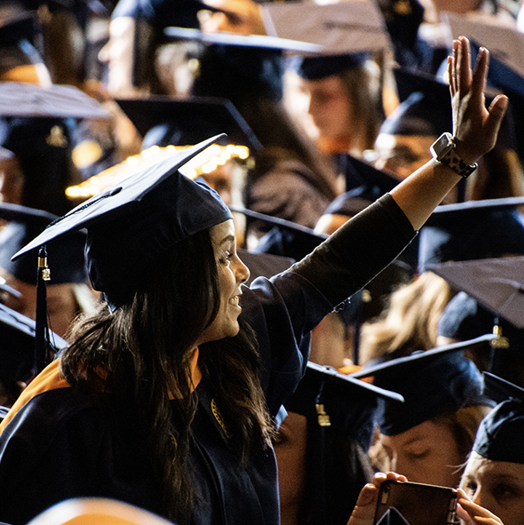 woman in cap and gown waving among a sea of fellow graduates