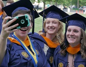 Three women dressed in blue and gold caps and gowns taking a selfie.