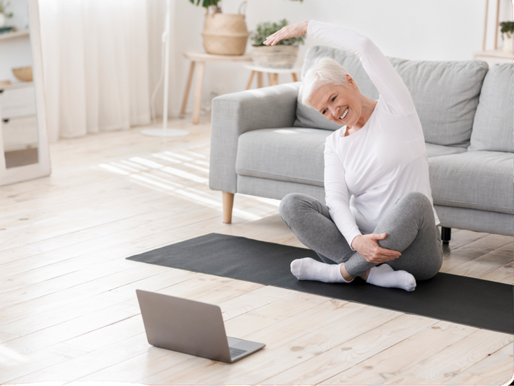elderly woman on yoga mat stretching in front of open laptop