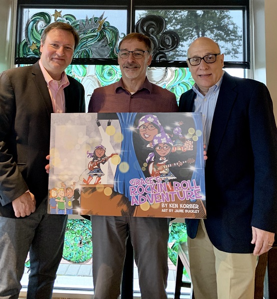 Ken Korber (center) with Eckhartz Press publishers Rick Kaempfer and David Stern holding cover of Grace’s Rockin’ Roll Adventure.