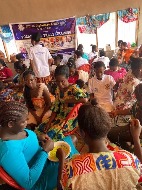 Ghanaian women sitting in groups learning how to bead.