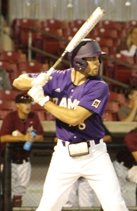 White male wearing a baseball uniform standing at bat.