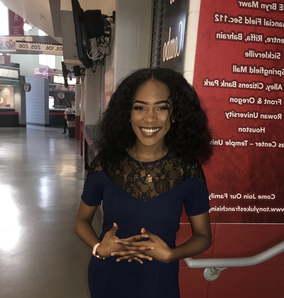 Young Black woman with long shoulder-length hair wearing a blue dress standing in the corridor of a ball park