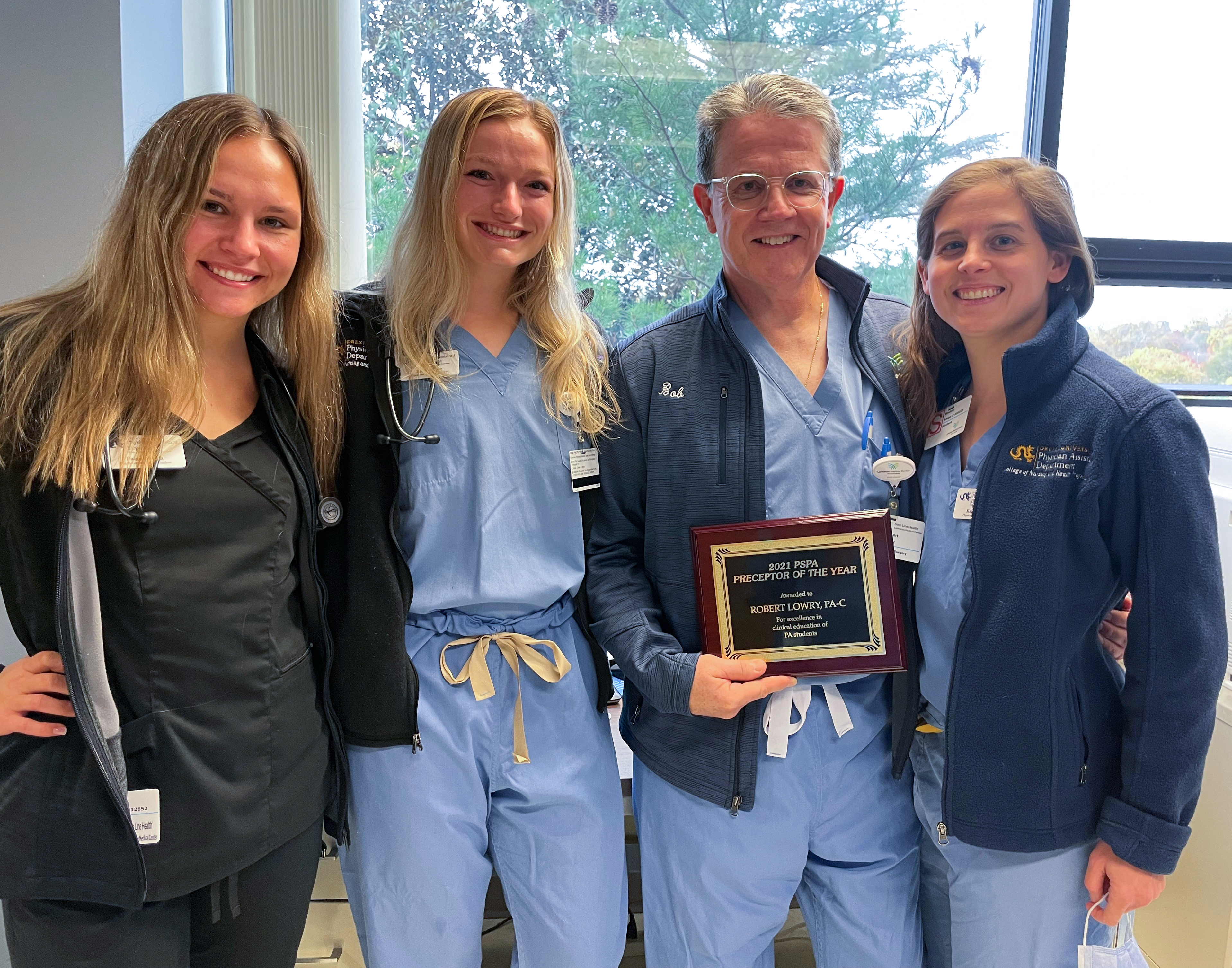 Bob Lowry, PA-C, a preceptor in the College of Nursing and Health Professions, holding his Preceptor of the Year award with three Drexel students. 