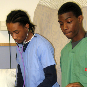 Two high school boys dressed in scrubs participate in hands-on simulation field experience.