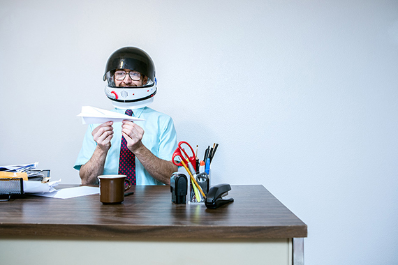 man at a desk wearing a helmet holding a paper airplane