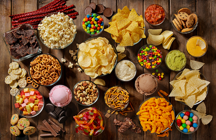Various junk foods, such as chips, candy and ice cream on a wooden table
